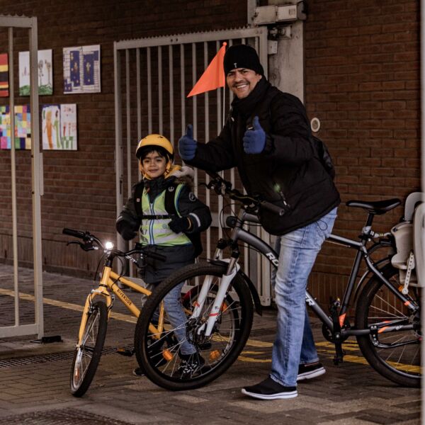 papa en zoontje met fiets steken duim omhoog aan de schoolpoort